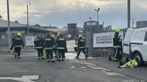 The image shows a eight uniformed members of the fire service standing outside the entrance to Plymouth Fisheries.