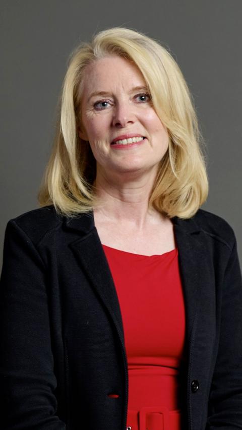 Woman with blond hair smiles for camera. She wears a black jacket over a red dress