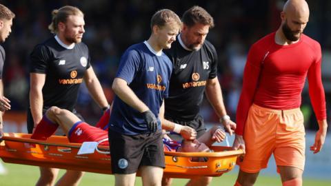 Ollie Harfield being stretchered off playing for Aldershot Town.