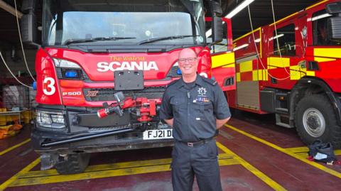 Julian Essex is pictured in front of a red fire engine
