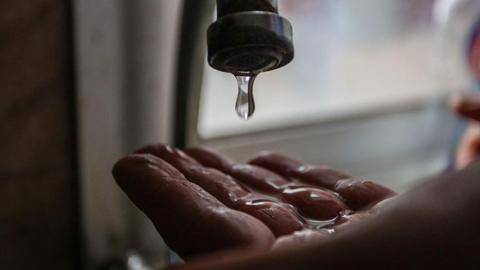 Water drips from a tap onto someone's hand. 