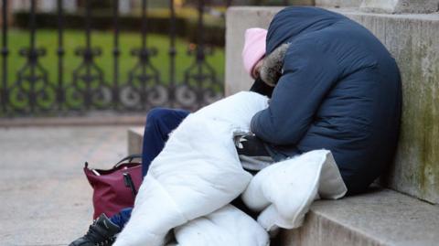 A person lying on a concrete step with a white blanket