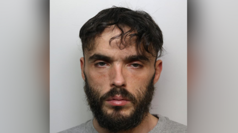 The mugshot of Matthew Haylett, who has short black hair and a black beard.