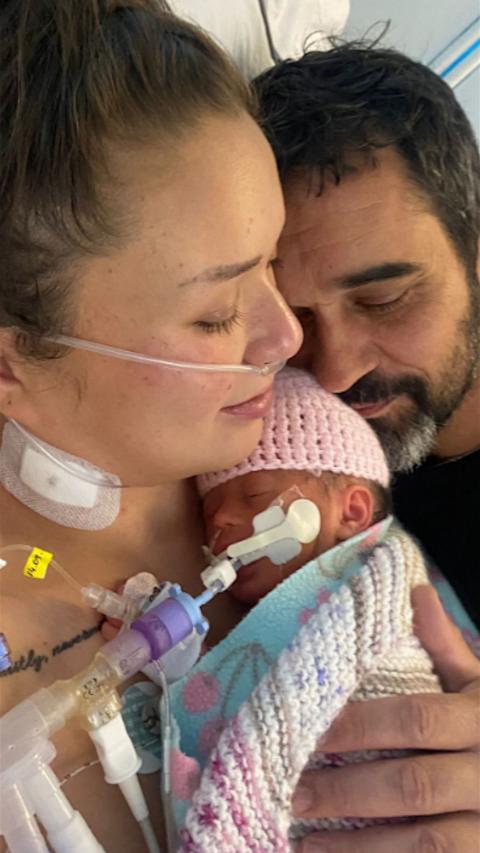 Woman with nose drip and bearded man cuddling a tiny newborn baby