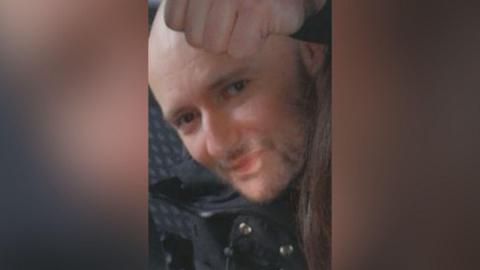 A bald man looking at the camera. He is wearing a black jacket. 
