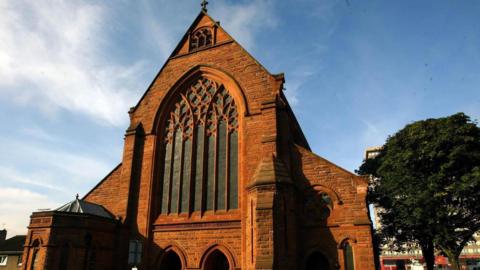A red stone church, in early decorated Gothic style, photographed on a bright sunny day. 