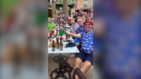 Racing fans dressed in Hawaiian shirts and sunglasses with their arms in the air.