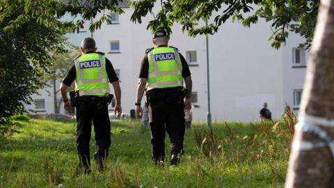Two police officers wearing high viz vests walk away from the camera