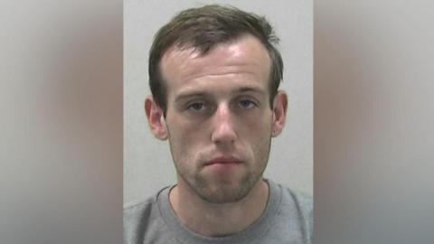 Mugshot of Reilly. He has very faint dark stubble and dark hair.