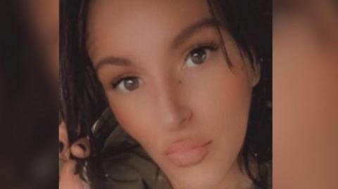 Close-up image of a woman with dark hair, looking straight at the camera.