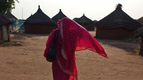 A Sudanese woman wearing pink walks through a village