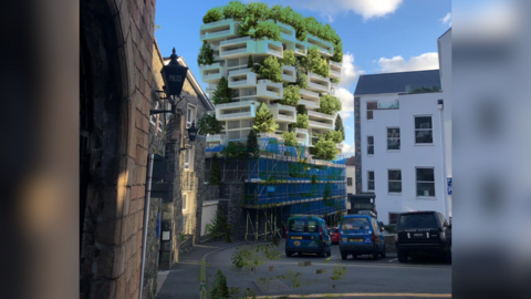 A computer generated image showing what a high rise building would look like next to Guernsey's police station. The AI building is the tallest in the picture and has greenery spread out in between storeys.