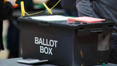 A black container on a table. The words 'ballot box' are written on the side.