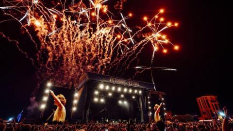 A stage with a large crowd. Screens show there is a performer on the stage, and writing above it reads "Victorious Festival". There are fireworks in the sky.