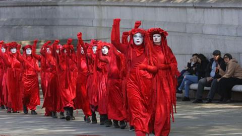 A line of women dress in red, each with a fist raised, protest in London against new oil and gas fields