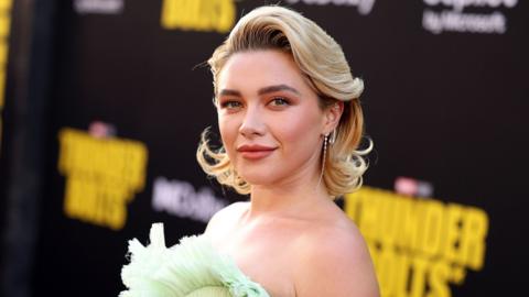 Florence Pugh wearing a green dress on the red carpet in front of a Thunderbolts* sign