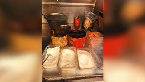 A silver kitchen surface covered with open, dirty containers - three containing what looks like salt and others containing sauce and oils.