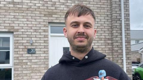 Man outside a house. He is wearing a dark-coloured hoodie