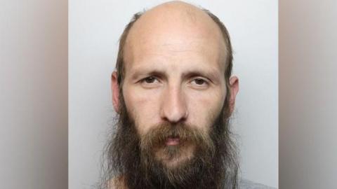 A custody photo of Tony James who has a brown beard. He is looking directly at the camera.