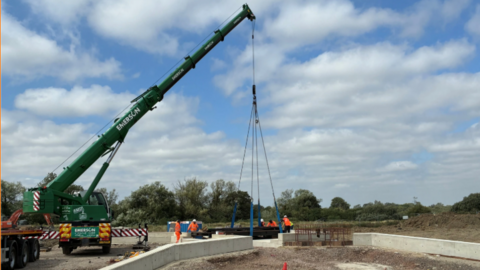 A crane being used to carry a bridge. Workers in high-vis jackets surround it.