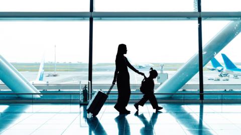 Woman and girl walks along airport window with planes in background