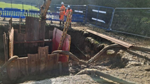 Large hole in a field with Thames Water workers standing at the edge - a digger and fencing are set up on the side.