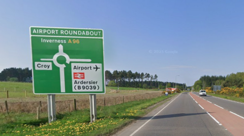 a sign saying Airport Roundabout stands next to a two-lane road