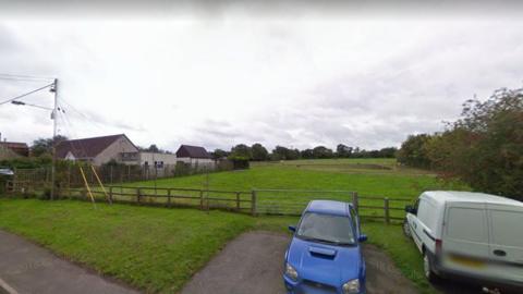 A photo of a field with two cars parked next to it