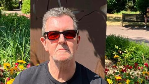 XTC super-fan Mike Smith sits in front of the new artwork while wearing sunglasses.