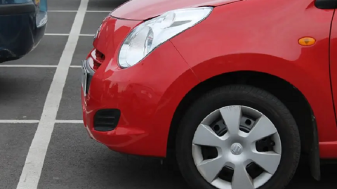 A close up picture of a red car in a car park. 