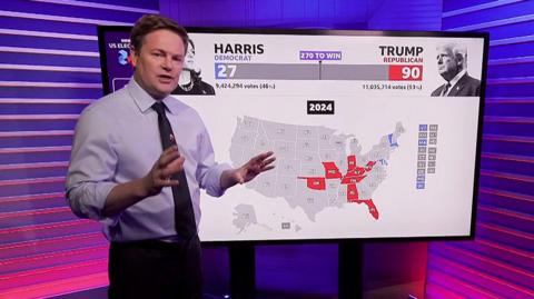 Christian Fraser standing and to his right, a touchscreen with a US map showing possible election results