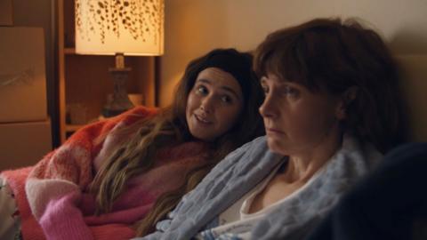 A woman, Billie, smiles at her mum, Deb, who looks sad in bed