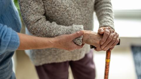 Senior woman with walking stick getting support from nurse, close-up - stock photo