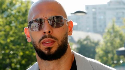 A shot of Andrew Tate from the shoulders up showing him outside wearing a pair of sunglasses.