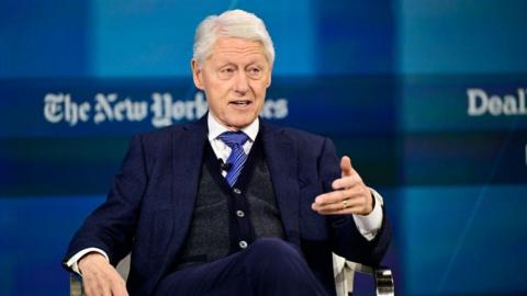 Bill Clinton gesturing while sitting in a chair during a lecture