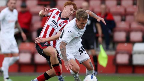 Ethan Galbraith of Swansea City is tackled by Harry Tustin of Cheltenham Town