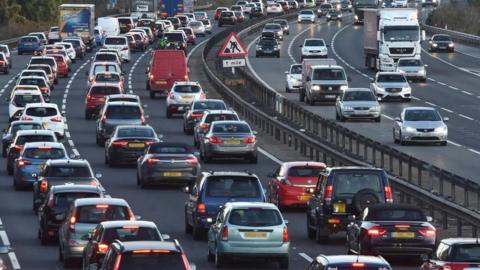 Traffic jam on a motorway, with a sign saying there are roadworks one mile ahead
