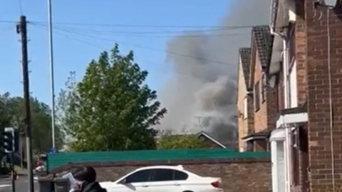 A large plume of smoke rises above some residential houses