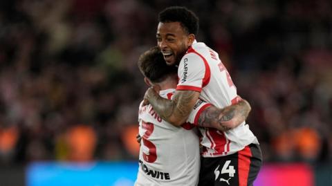 Two footballers players embrace as they celebrate winning a place in a play-off final