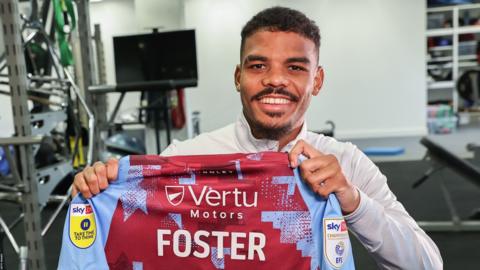 New signing Lyle Foster holding up a Burnley FC shirt bearing his name.