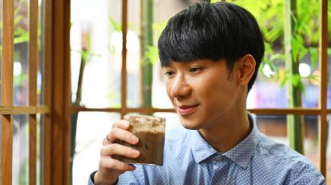Young man holds a glass of hojicha.