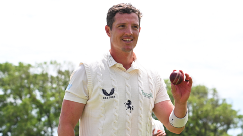 Keith Dudgeon, wearing Kent whites, holds up the ball at the end of the Lancashire innings to celebrate taking six wickets