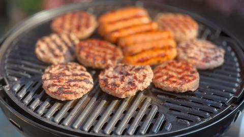 A metal grill with round burger meat patties being grilled on it.