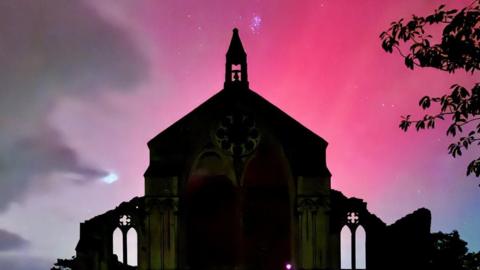 A pink sky is seen behind a silhouette of Binham Priory, Norfolk