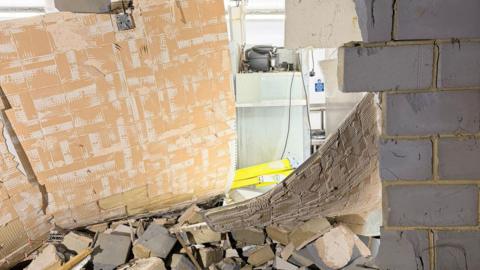 A collapsed wall looking into a kitchen with bricks and rubble on the floor.