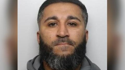 Mugshot of rapist Amar Khan, 42, who has black hair and a black and grey beard.