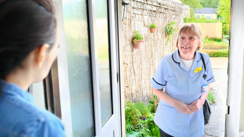 A Dorothy House Hospice Care staff member on the doorstep speaking to a woman at her home.