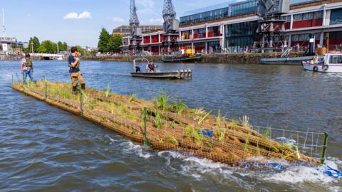 A 17 metre long island, made from recycled plastic water pipes, being launched into the river