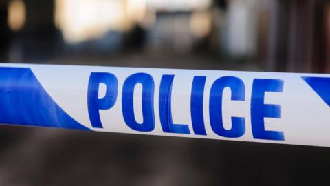 Stock image of crime scene tape. It is white and blue, with "Police" written on it.