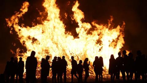 A number of people are silhouetted in the flames of a bonfire